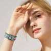 Una mujer usando una banda deportiva elástica con estampado verde y rosa en su muñeca.