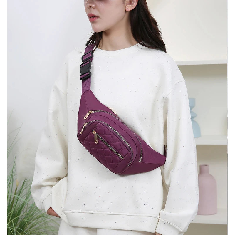 Une femme porte un sac à bandoulière en nylon rembourré violet sur son sweat blanc.