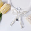 A clear pearl bow keychain with a heart charm resting on a white ceramic object next to a yellow tulip.