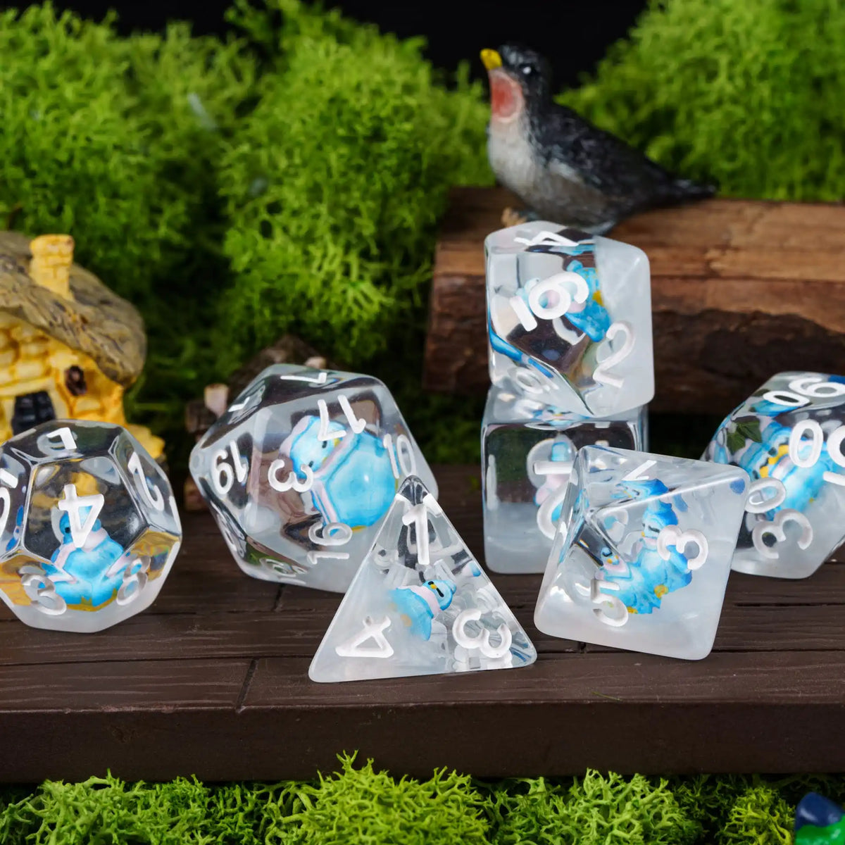 A set of clear resin dice shaped like animals and geometric solids, displayed in a natural setting with greenery.
