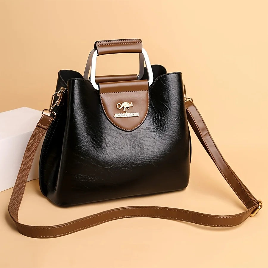 A black leather vintage crossbody tote bag with brown trim and a gold-toned hardware is shown on a light background.
