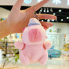 A hand holds a pink capybara plush toy with a yellow duck swim ring against a blurred indoor background.