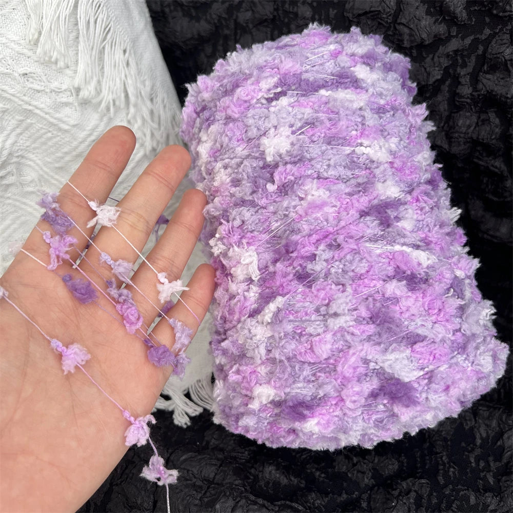 A hand holds a ball of purple and white variegated yarn for knitting or crochet.