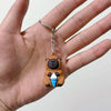 A small brown capybara charm keychain is being held in a person's hand.