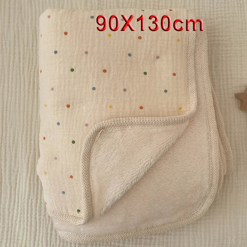 A beige floral muslin baby blanket with a ribbed edge is shown folded on a light background.
