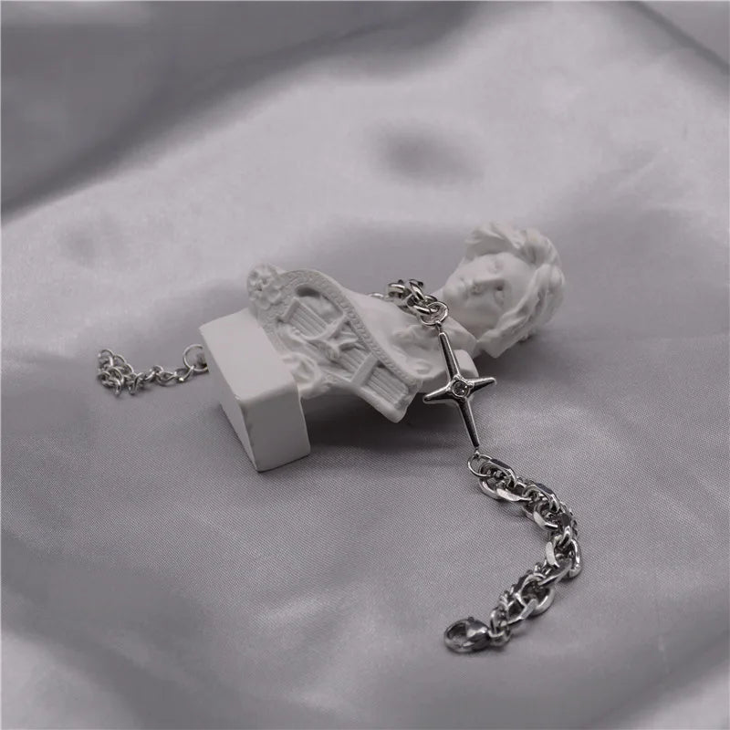 Bracelet en argent à double couche, étoile et croix, posé sur un tissu satiné gris.