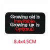 Black iron-on letter patch with red embroidered text that reads Growing old is inevitable Growing up is optional