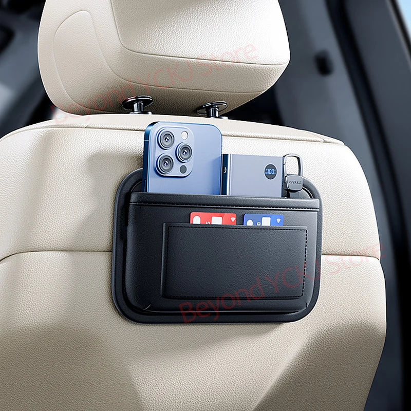 A black storage organizer bag with a clear window holds a smartphone and a small accessory, mounted on a light-colored car se