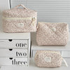 A set of three vintage floral quilted cosmetic bags in light pink and cream colors displayed on a white shelf.