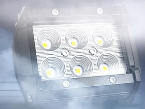 A close-up view of an 18W LED flood light pod pack with four bright lights inside, surrounded by mist.