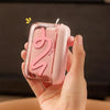 A hand holds a pink portable automatic floss pick dispenser with a pop-up mechanism.