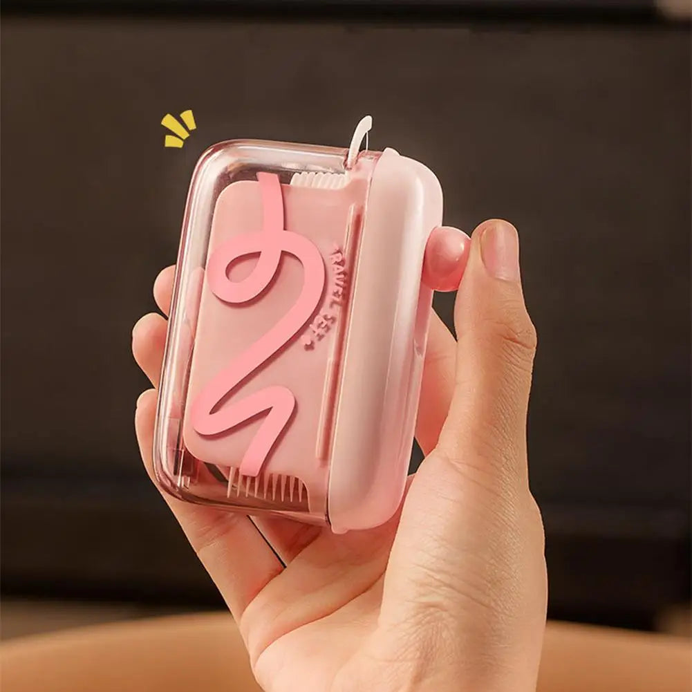 A hand holds a pink portable automatic floss pick dispenser with a pop-up mechanism.