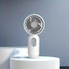 A white handheld fan with a silver grille is displayed on a round white pedestal against a gray background.
