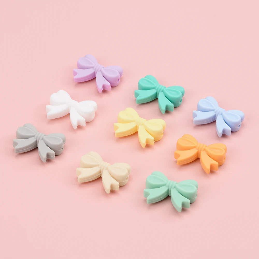 A collection of pastel silicone crown beads in lavender, mint green, pale yellow, and light blue scattered on a pink backgrou