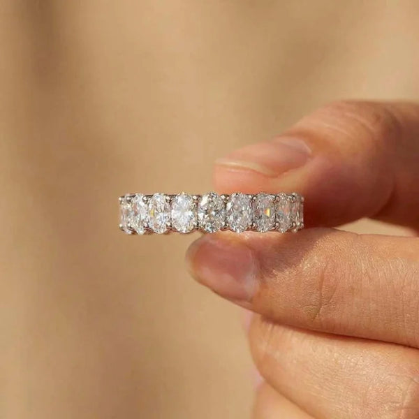 A hand holds an oval cubic zirconia sterling silver ring with a row of small stones.