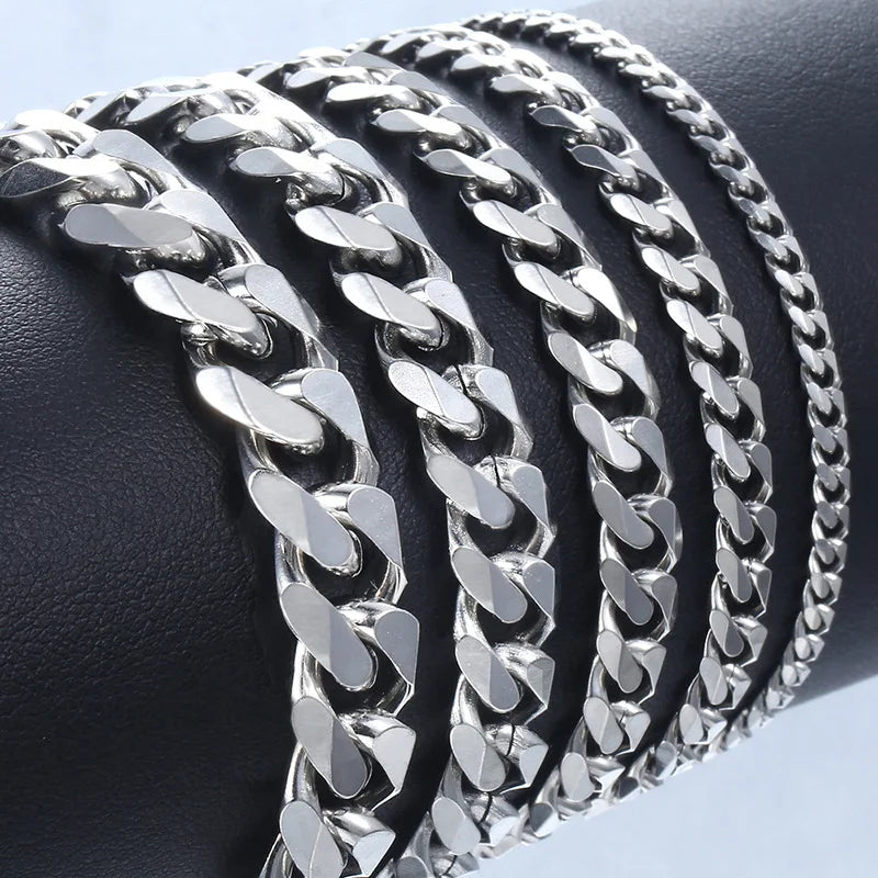 A close-up of a black wrist wearing multiple silver stainless steel Cuban link bracelets.