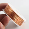 A hand holds a coil of bare copper wire with multiple diameters, showing the shiny golden color.