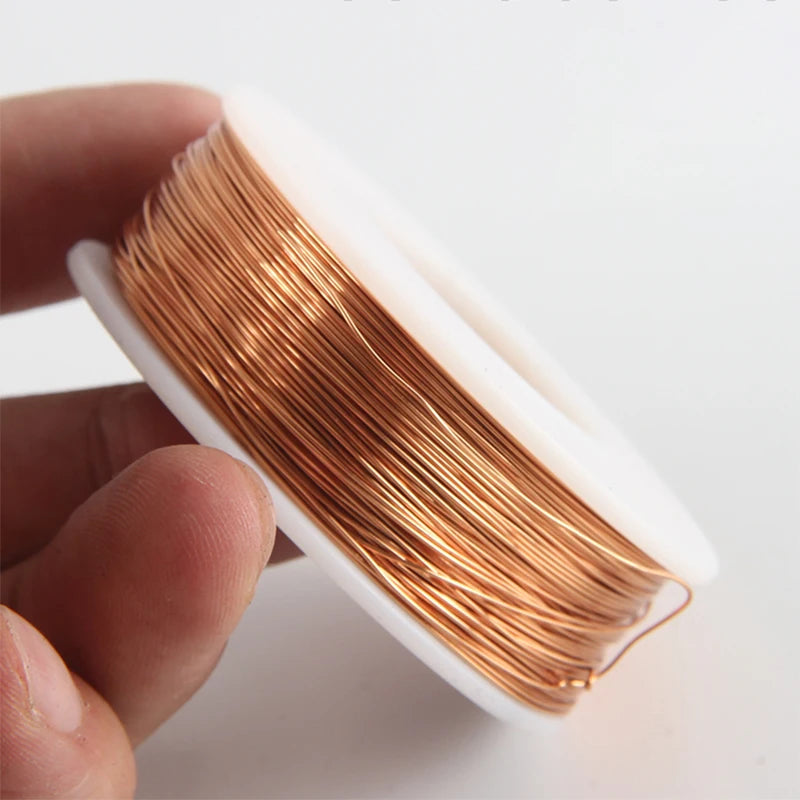 A hand holds a coil of bare copper wire with multiple diameters, showing the shiny golden color.