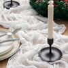 A white crinkle gauze cheesecloth table runner is displayed on a wooden surface with silverware and a tall white candle.