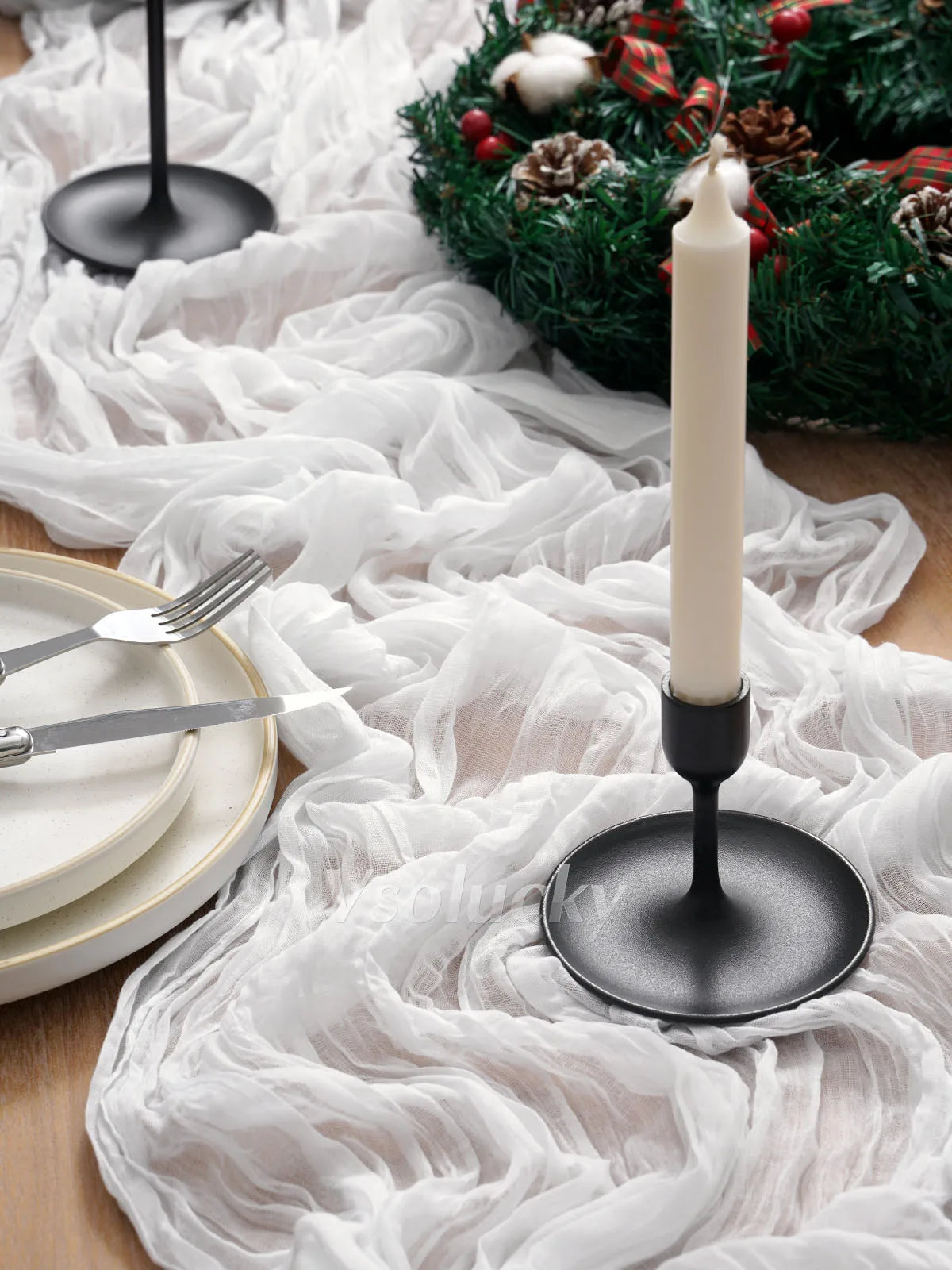 A white crinkle gauze cheesecloth table runner is displayed on a wooden surface with silverware and a tall white candle.