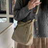 A woman holds a beige matte leather crossbody hobo bag with an adjustable strap against a light background.