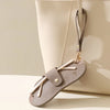 A light beige leather glasses case with a brown strap and a flap closure is shown against a neutral background.