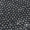 A close-up view of small black acrylic alphabet letter beads scattered on a white surface.