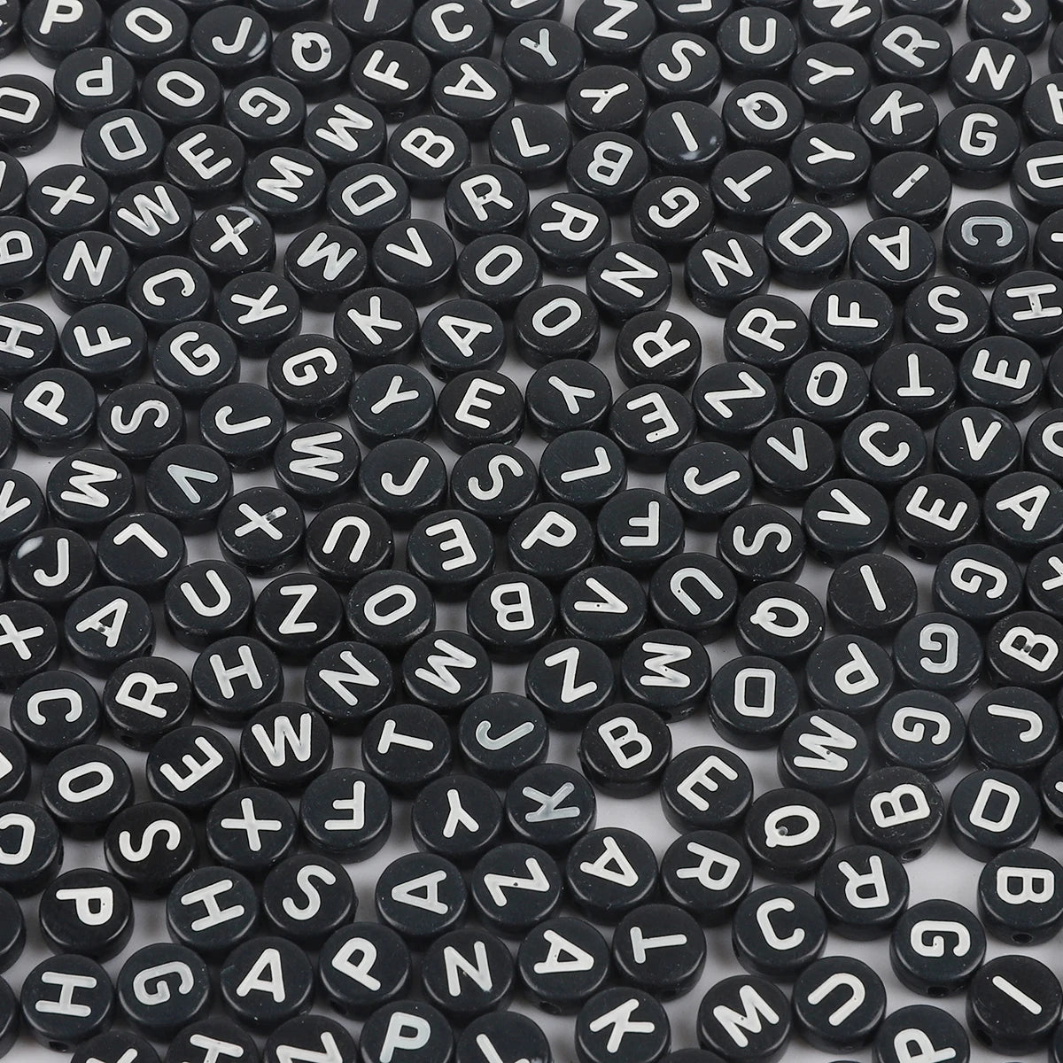 A close-up view of small black acrylic alphabet letter beads scattered on a white surface.