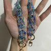 A close-up of a hand holding a long, iridescent blue and green resin chain replacement strap for a handbag.