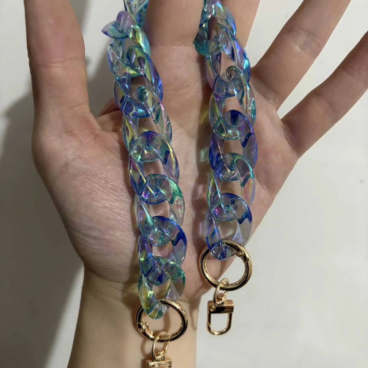 A close-up of a hand holding a long, iridescent blue and green resin chain replacement strap for a handbag.