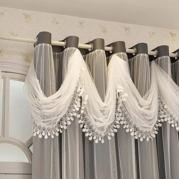 Gray sheer curtains with white lace trim are hung on a rod in a room.