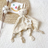 A cream-colored elephant plush toy with ears, a teether, and a striped blanket is resting on a woven mat.