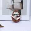 A wooden kalimba thumb piano with eight metal tines is displayed in a white frame.