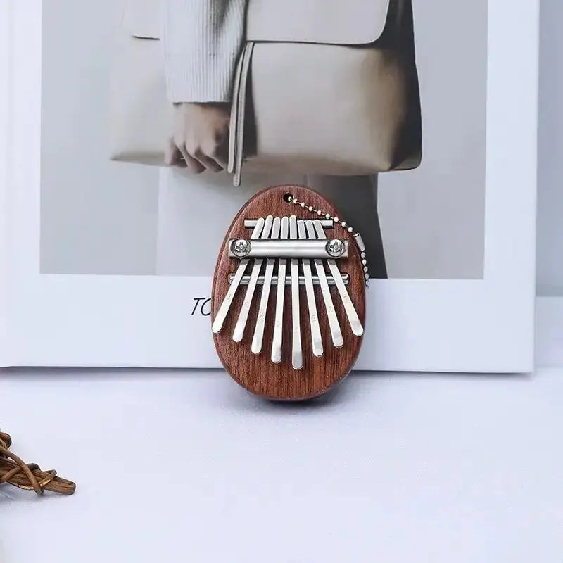 A wooden kalimba thumb piano with eight metal tines is displayed in a white frame.