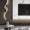 A modern minimalist LED wall lamp with a curved light fixture mounted on a dark gray textured wall.