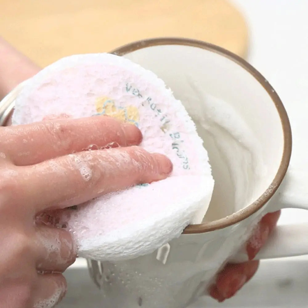 A hand is dipping a pink cotton scouring sponge into a white mug filled with liquid.