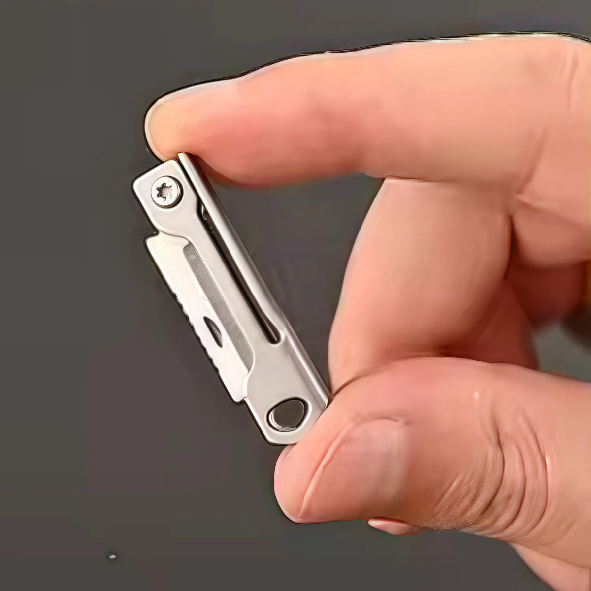 Une main tient un petit couteau de poche pliable, montrant sa lame et son mécanisme argentés.