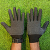A pair of black knitted work gloves with a dotted grip are shown on a person's hands against a green background.