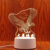 A white silhouette of an eagle with spread wings is illuminated by a light source, displayed on a wooden surface.