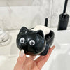 A hand holds a black cat-shaped soap box with a white drainage tray against a white bathroom background.