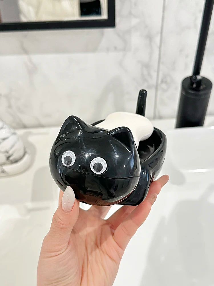 A hand holds a black cat-shaped soap box with a white drainage tray against a white bathroom background.