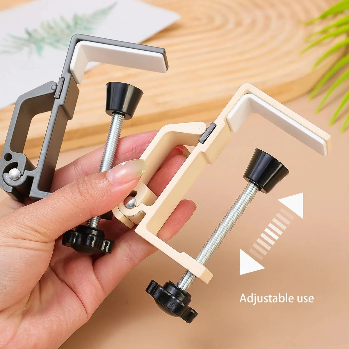 A hand holds a foldable aluminum desk hook with a silver screw and black grip, demonstrating its adjustable use.