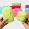 A hand holds a lime green portable soap holder with a lid, surrounded by other colored versions.