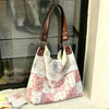 Sac à l'épaule patchwork rose et blanc avec motifs floraux et sangles en cuir marron, exposé devant une fenêtre.