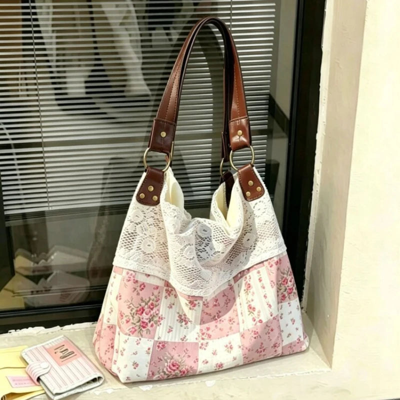 Sac à l'épaule patchwork rose et blanc avec motifs floraux et sangles en cuir marron, exposé devant une fenêtre.