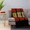 A knit throw blanket featuring the NFL team logo in red, gold, and black on a gray sofa.