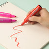 A hand is applying red washable scented markers to a piece of paper, demonstrating the product.