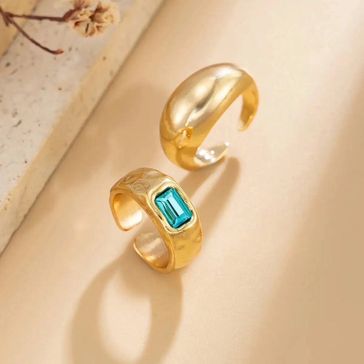 Gros plan d'une bague au doigt en or avec un cristal bleu carré sur fond clair.