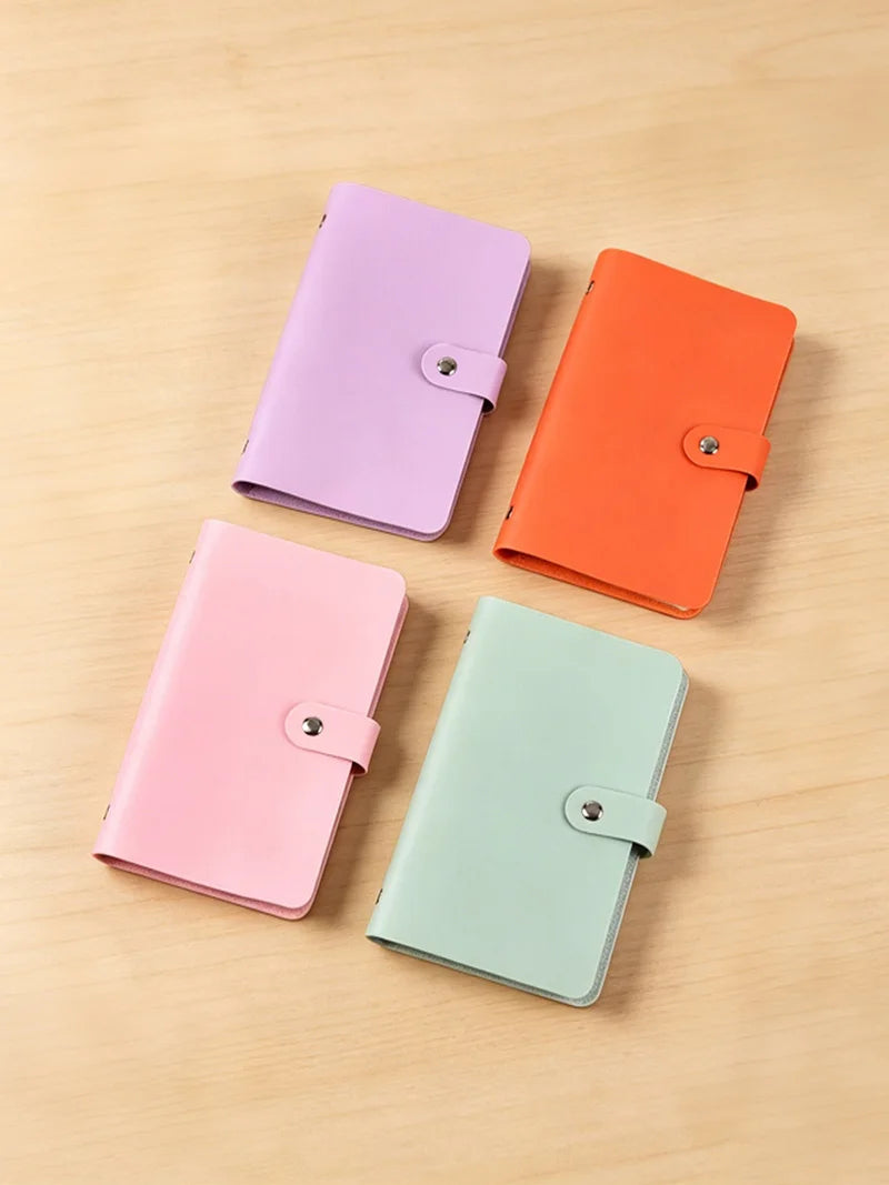 Four colored cash organizer binders in purple, orange, pink, and mint green with snap closures on a wooden surface.