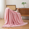 A fluffy pink brushed flannel throw blanket draped on a wooden table next to a plant.